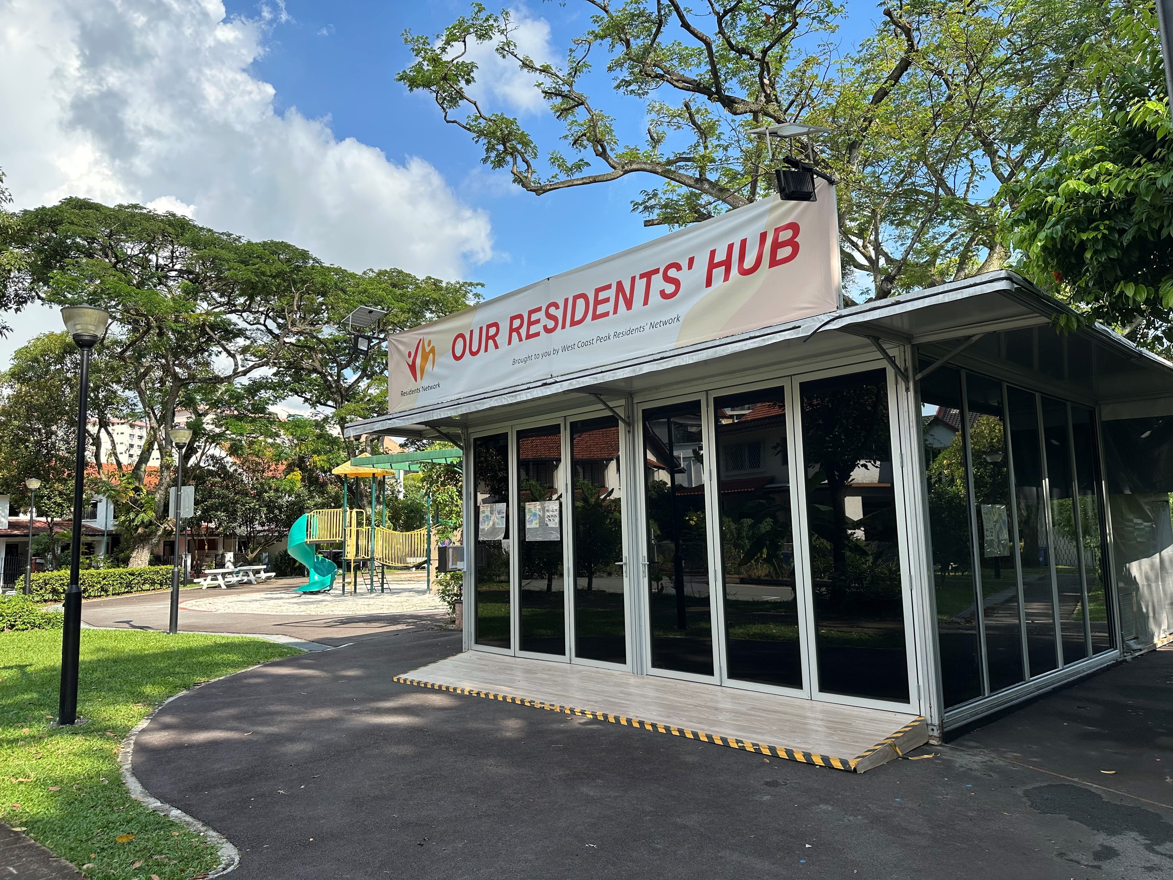 "Our Residents' Hub" building in a park. Playground visible in the background.